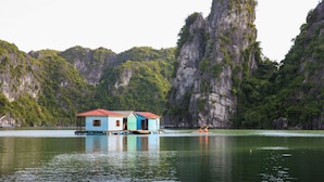 A floating house with a red roof and blue walls, surrounded by calm water and steep cliffs. - Imperial Legend Cruise Halong (Tuan Chau)