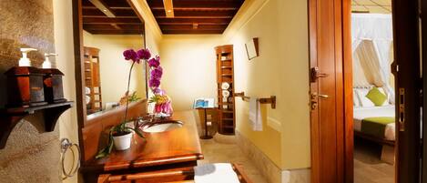 A bathroom with a wooden vanity, a towel rack, a mirror, and a bed with a white canopy.