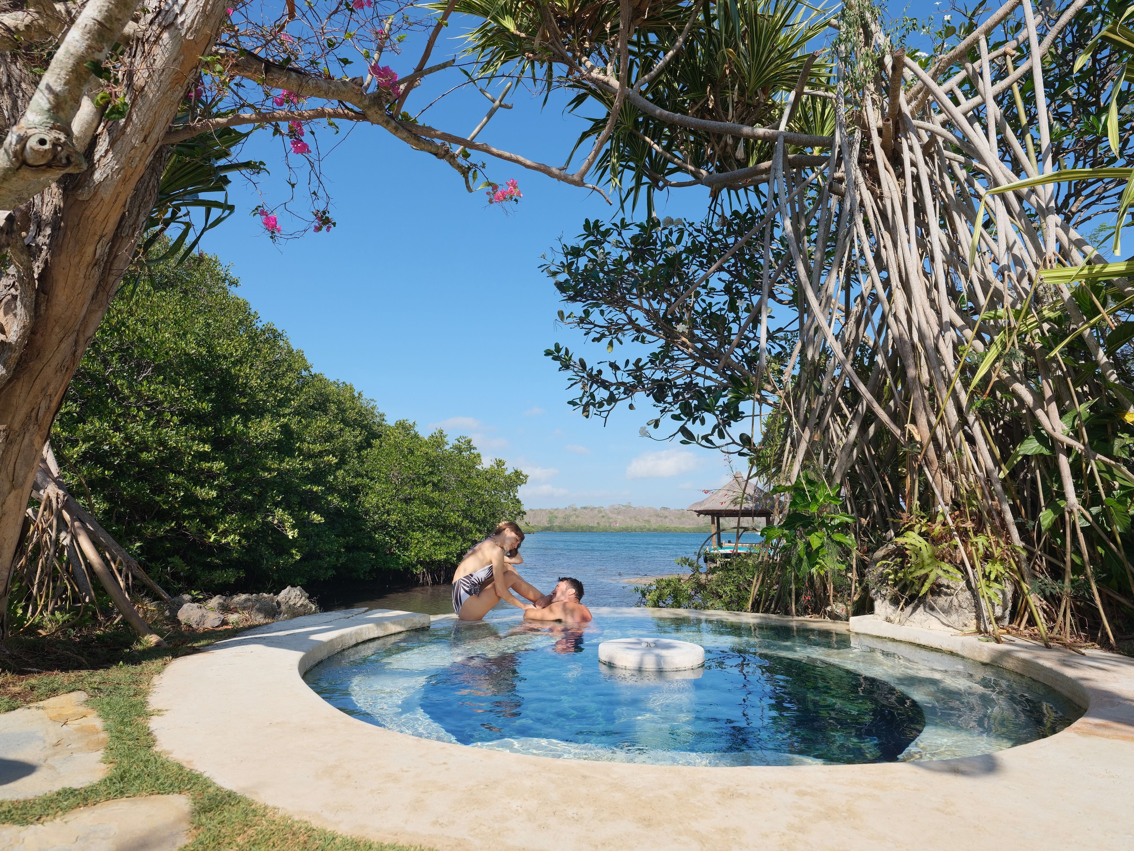 A circular pool with a concrete edge, surrounded by lush greenery and a clear view of the sea.