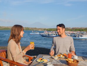 A couple dining at a table with a view of boats and a mountain in the background. - Mimpi Resort Menjangan (Pejarakan)