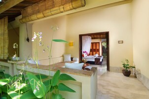 Una habitación de hotel con una cama, una zona de estar con una mesa y sillas, y una planta en maceta.
