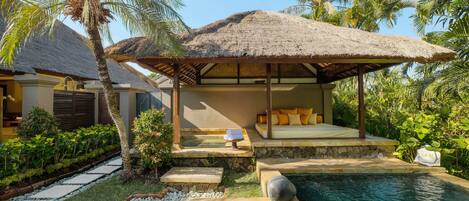 A thatched-roof outdoor seating area with a stone bench and a small pool.
