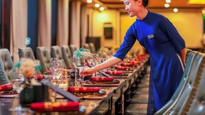 Un miembro del personal de hotel preparando una mesa de comedor con cristalería y cubertería.
