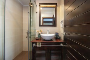A bathroom with a glass shower enclosure, a white sink, and a dark wooden vanity.