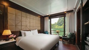 Habitación de hotel con una cama grande, una mesita de noche con lámpara, una silla y vistas a un lago desde la ventana.