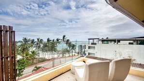 Un balcon doté de meubles en osier, d’une rambarde en verre et offrant une vue sur la plage et les palmiers.