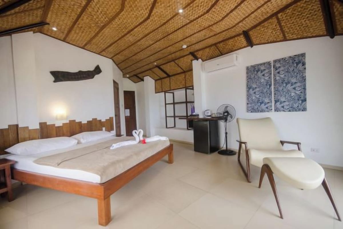 A bedroom with a wooden bed, a chair, a desk, and a fan.