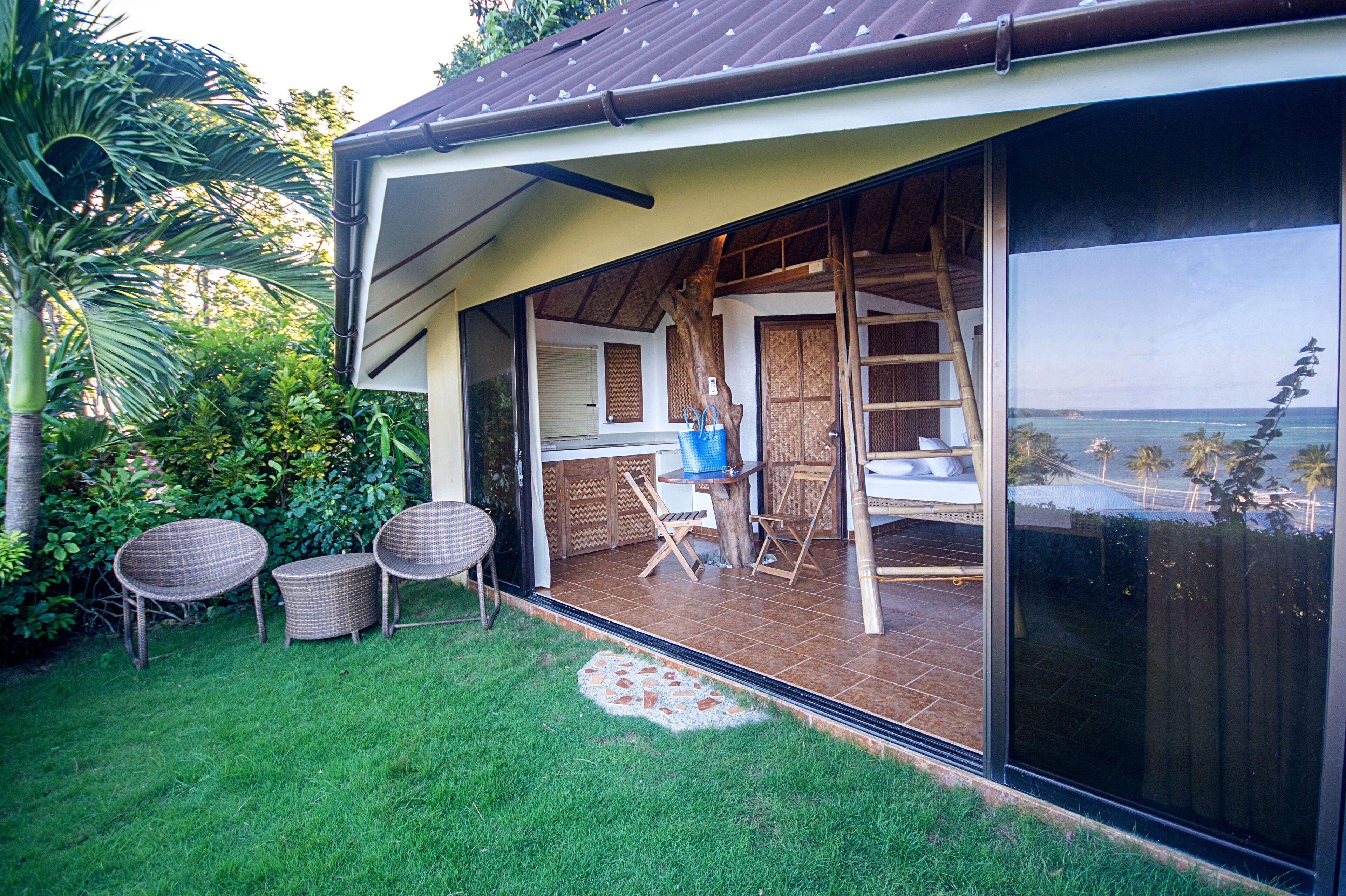 A covered outdoor area with a view of the ocean, a wooden deck, and wicker chairs.