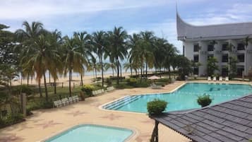 A pool area with palm trees, a beach, and a building with a unique roof design.