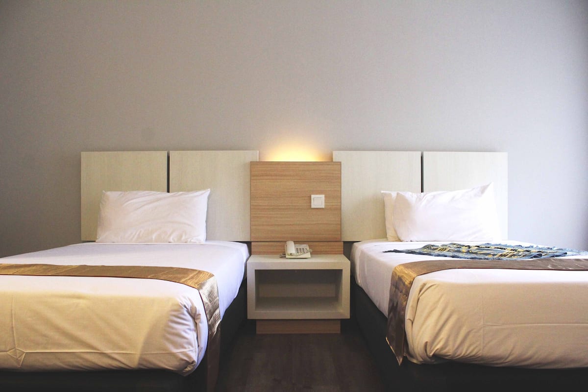 Ein Hotelzimmer mit zwei Einzelbetten, einem hölzernen Kopfteil und einem Nachttisch mit Telefon.