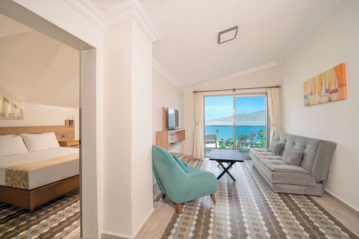 A hotel room with a bed, a sofa, a TV, a balcony with a view, and patterned flooring.