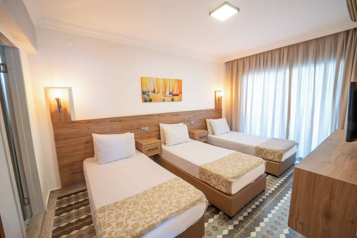 A hotel room with three single beds, a wooden headboard, a painting on the wall, and a television.