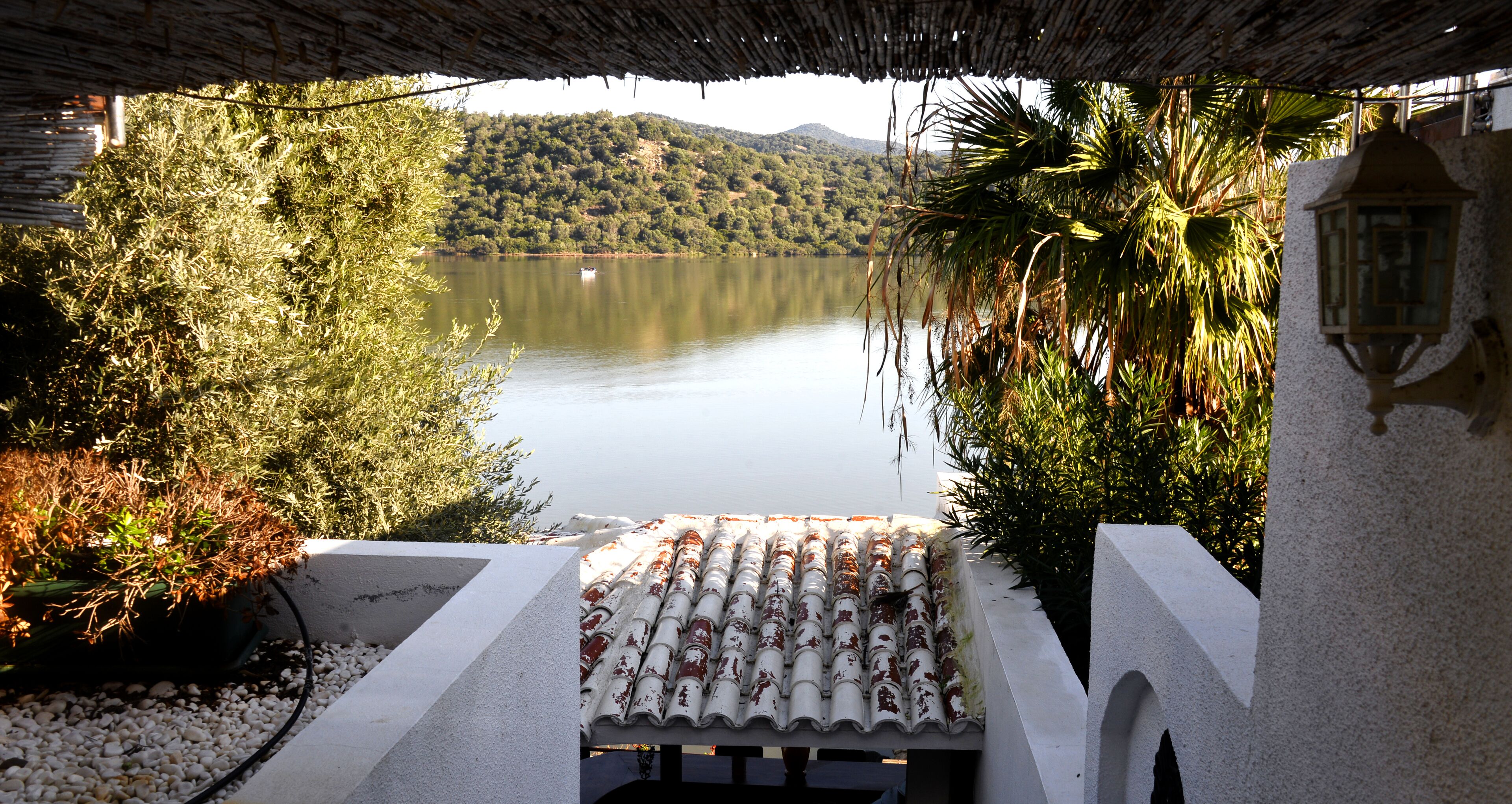 Une vue d’un lac, avec un toit recouvert de tuiles et un mur blanc surmonté d’une arche.