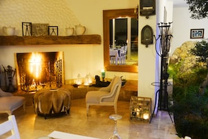 Una sala de estar acogedora con chimenea, asientos cómodos y un comedor visible a través de un vidrio.
