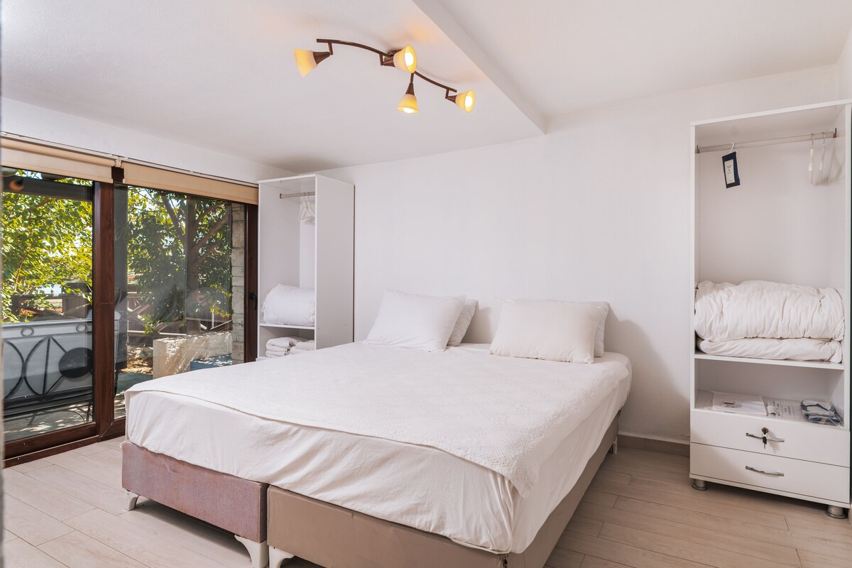 A bedroom with a large bed, a wardrobe, and a sliding glass door to a balcony.