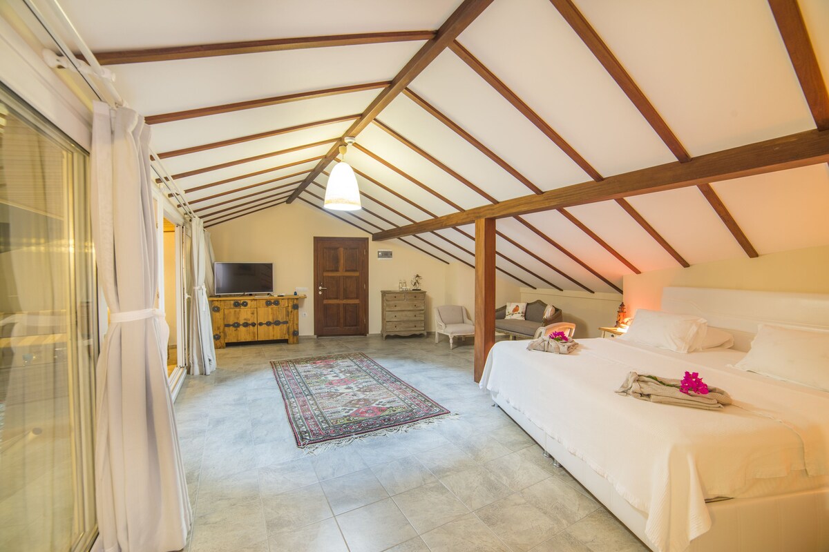 A bedroom with a sloped ceiling, a bed, a TV, a dresser, and a rug.
