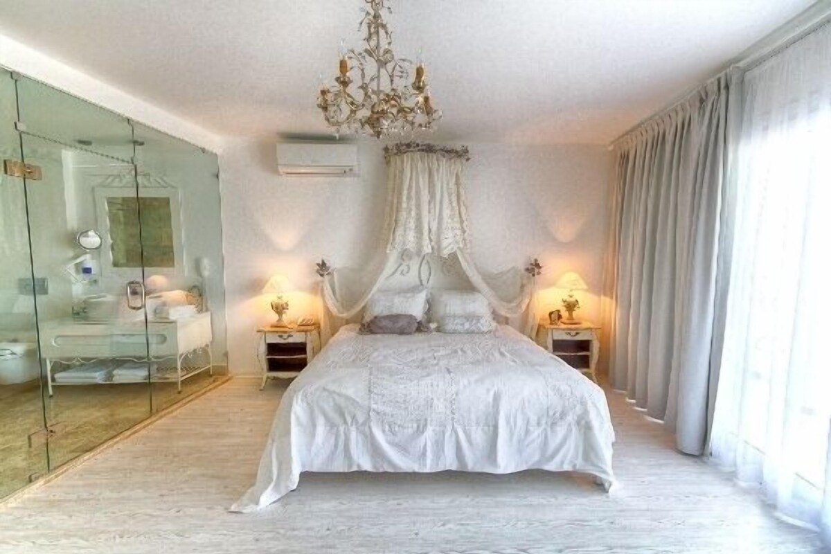 A bedroom with a canopy bed, glass shower enclosure, and bedside lamps.