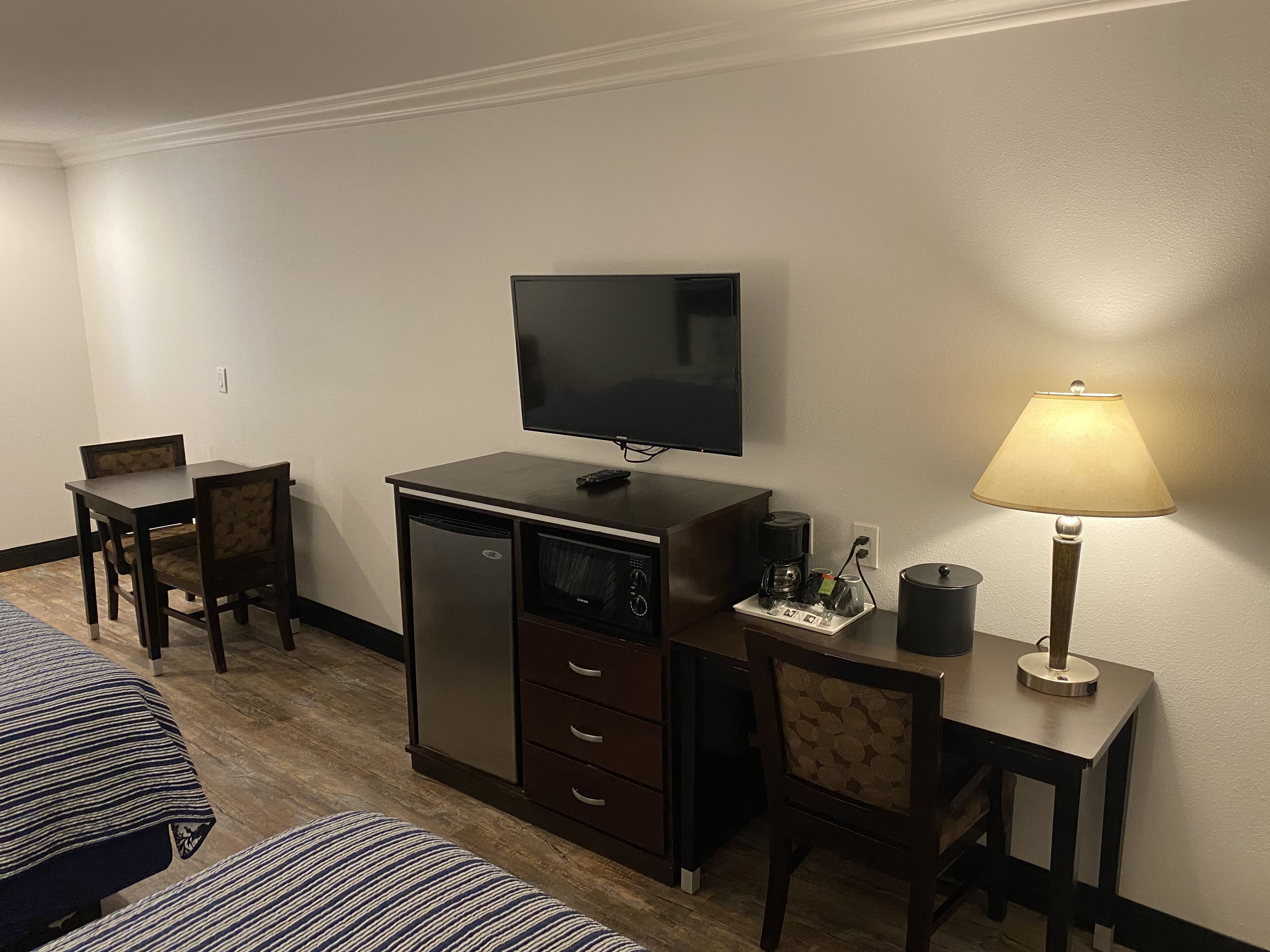 Habitació d'hotel amb llit, escriptori amb làmpada, televisió, cafetera i nevera petita.
