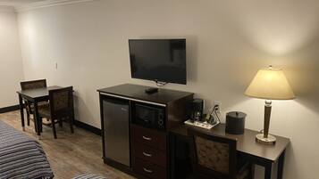 Habitació d'hotel amb llit, escriptori amb làmpada, televisió, cafetera i nevera petita.