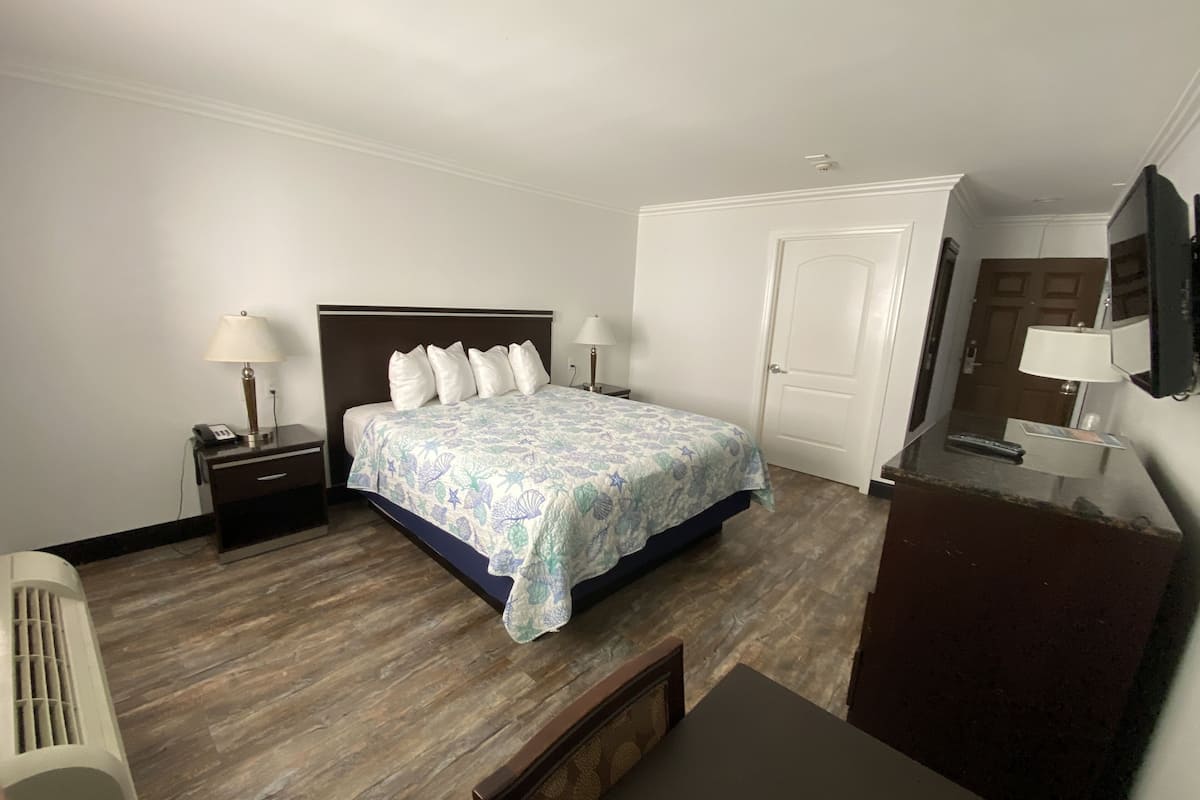 A hotel room with a bed, bedside tables, a desk, a chair, a TV, and a door.