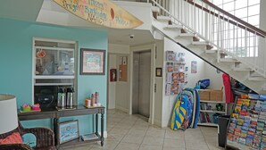 A room with a staircase, a table with thermos flasks, a welcome sign, and a wall with various items including a surfboard. - Ocean Surf Inn & Suites (Huntington Beach)