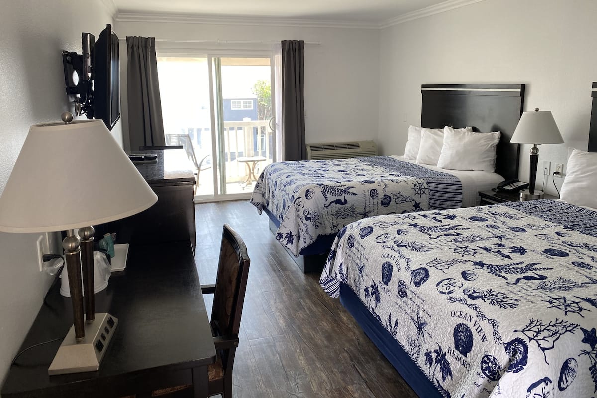 A hotel room with two beds, a desk, a chair, a TV, and a balcony with curtains.