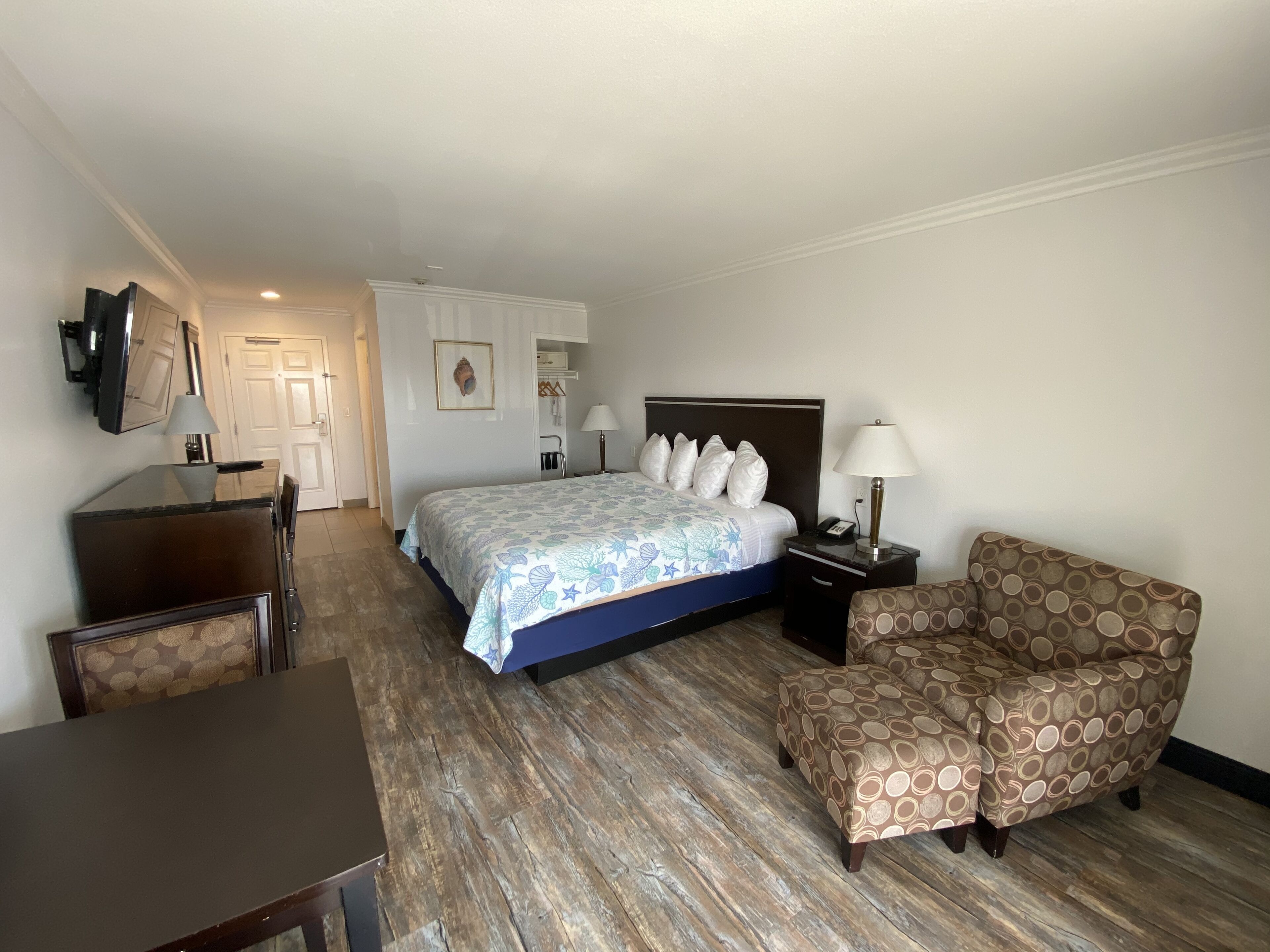 A hotel room with a bed, a desk, a chair, and a sofa.