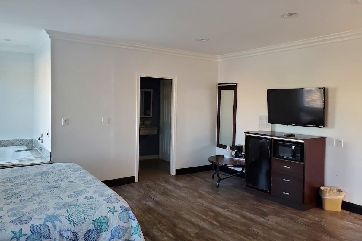 A hotel room with a bed, a desk, a television, a mirror, and a trash can.