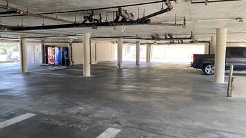 A parking garage with concrete pillars, visible pipes, and a parked SUV.