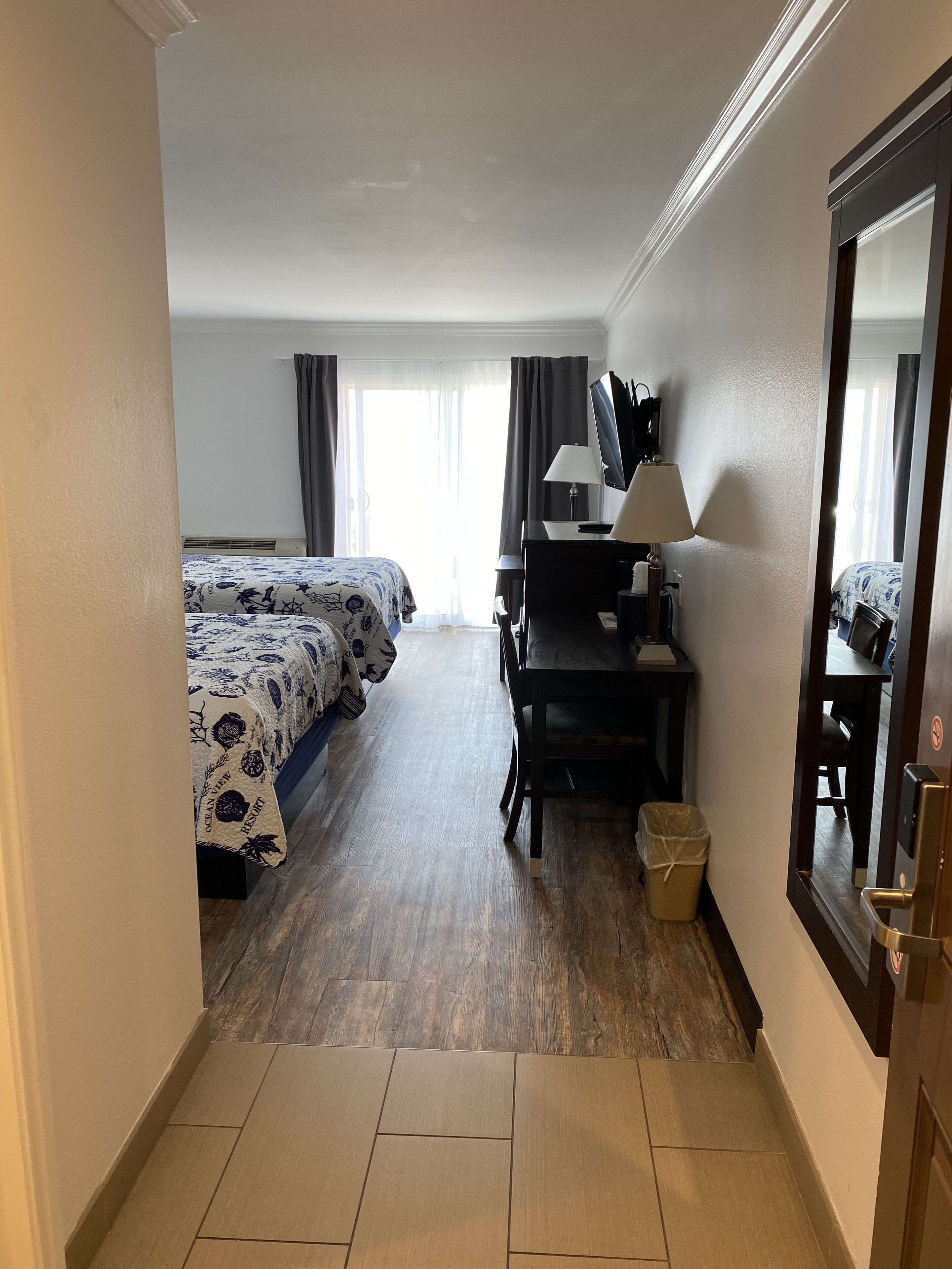 Ein Hotelzimmer mit zwei Betten, einem Schreibtisch, einem Stuhl, einem Fernseher und einem Fenster mit Vorhängen.