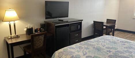 Una camera d'albergo con un letto, una scrivania con una lampada, una televisione, un forno a microonde e una sedia.