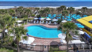 A pool area with lounge chairs and umbrellas, surrounded by palm trees, with a view of the ocean. - Seahorse Oceanfront Inn (Neptune Beach)