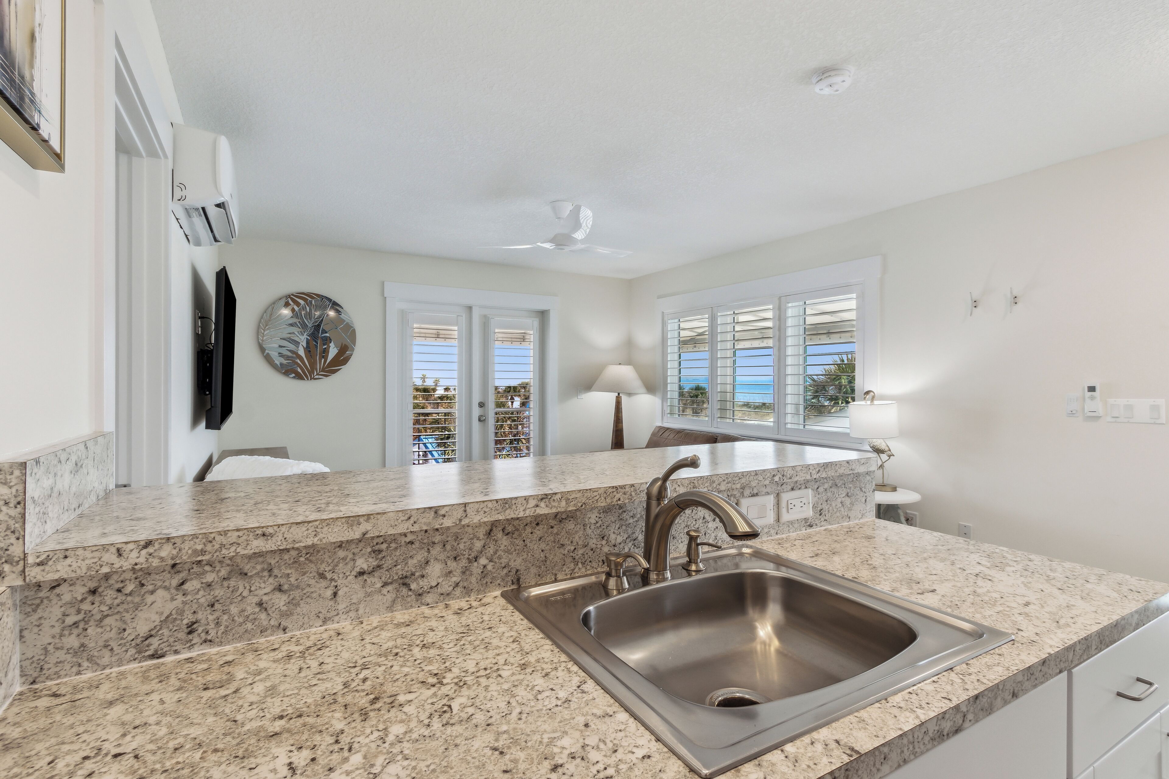 A modern kitchen with granite countertops, a stainless steel sink, and a ceiling fan.