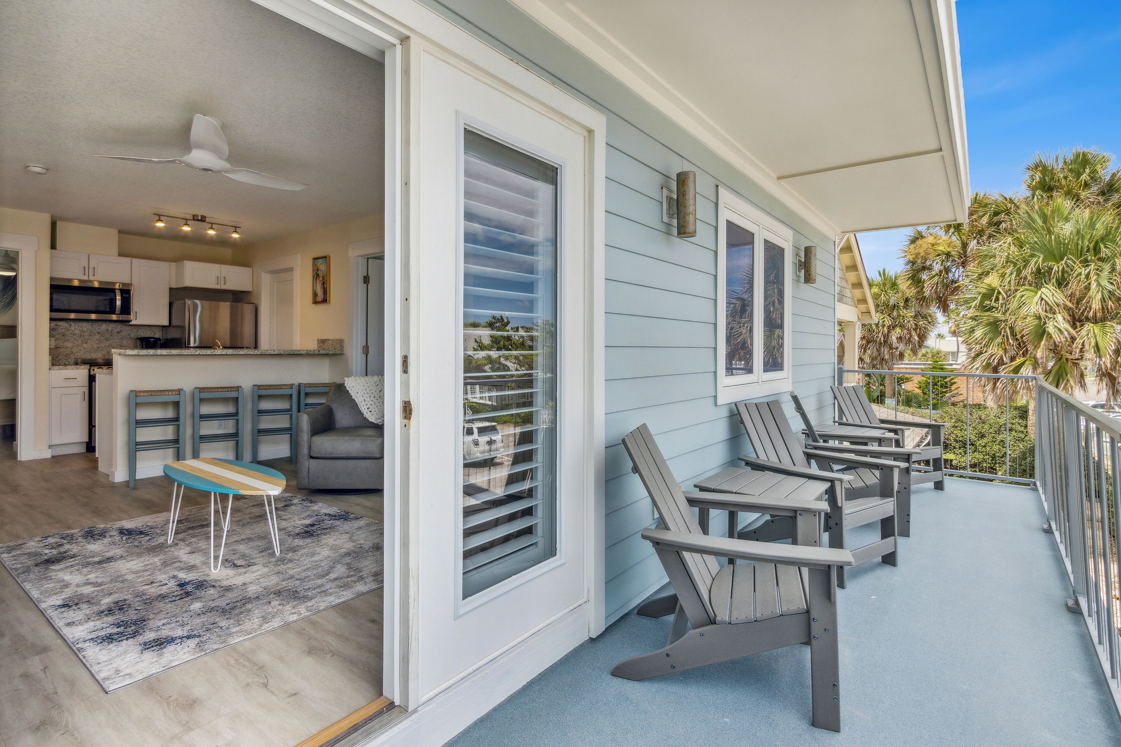 A covered porch with Adirondack chairs and a dining table.