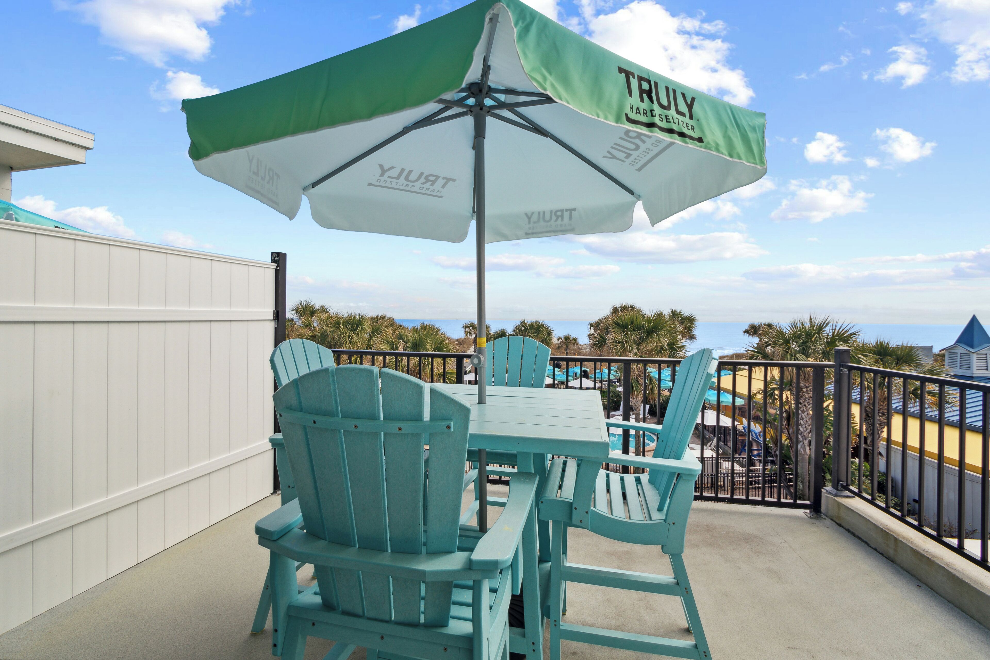 A patio with turquoise Adirondack chairs and a table under a green and white umbrella with "TRULY" branding.
