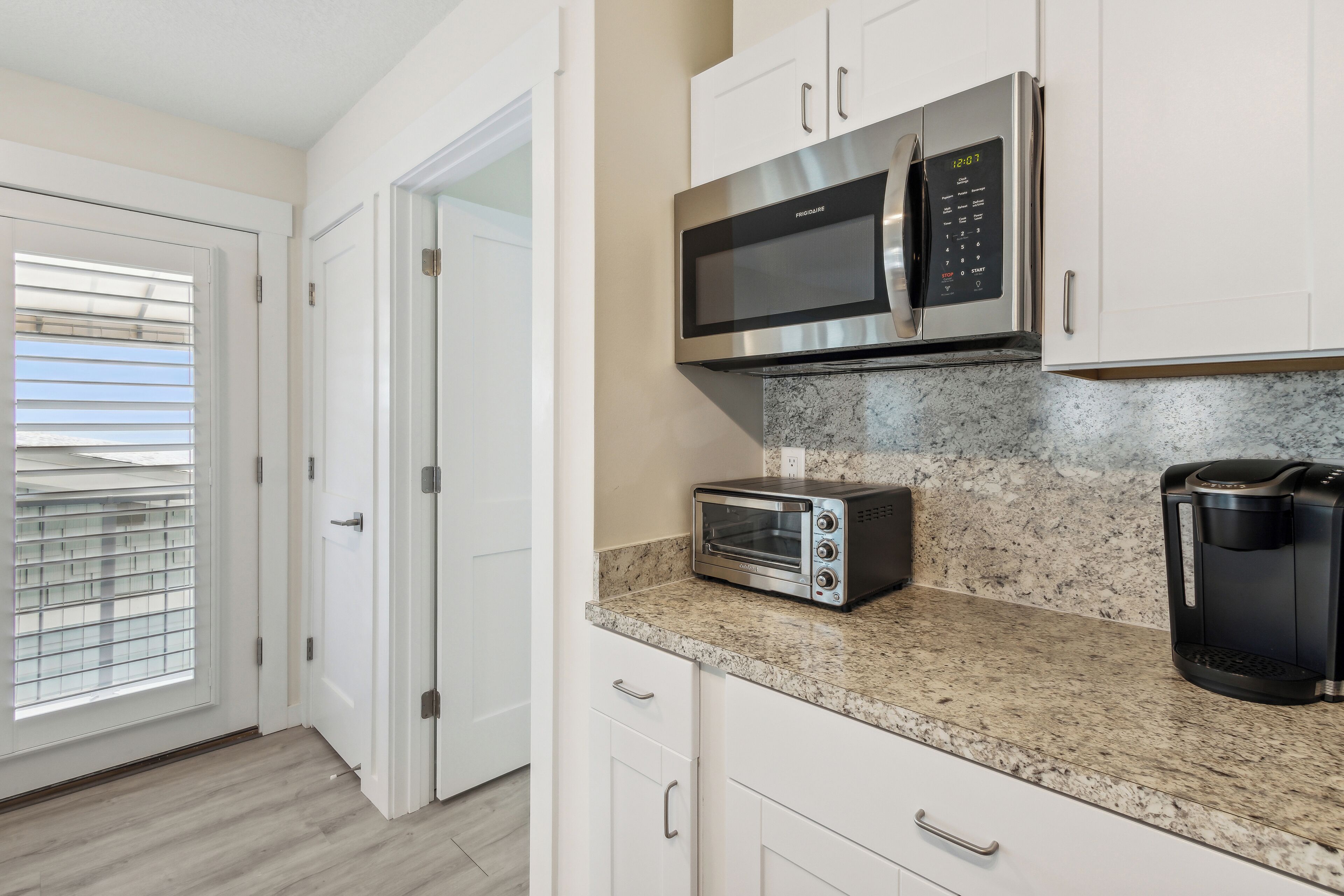 A modern kitchen with white cabinets, a stainless steel microwave, a toaster, and a coffee maker on a granite countertop.