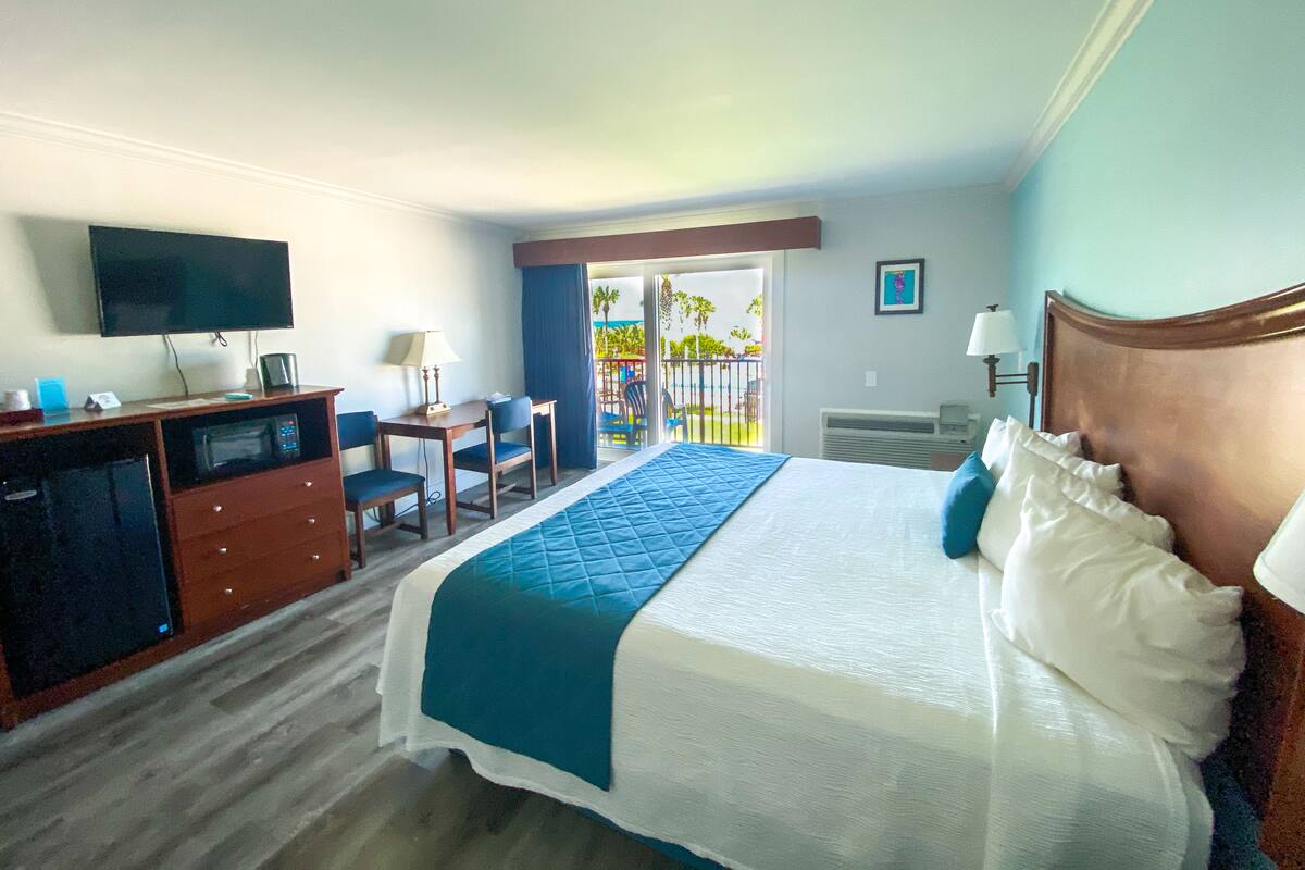 A hotel room with a bed, desk, chair, TV, and a balcony with a view.