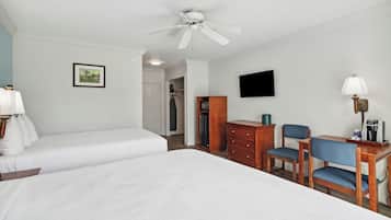 A hotel room with two single beds, a desk with a chair, a television, and a ceiling fan.