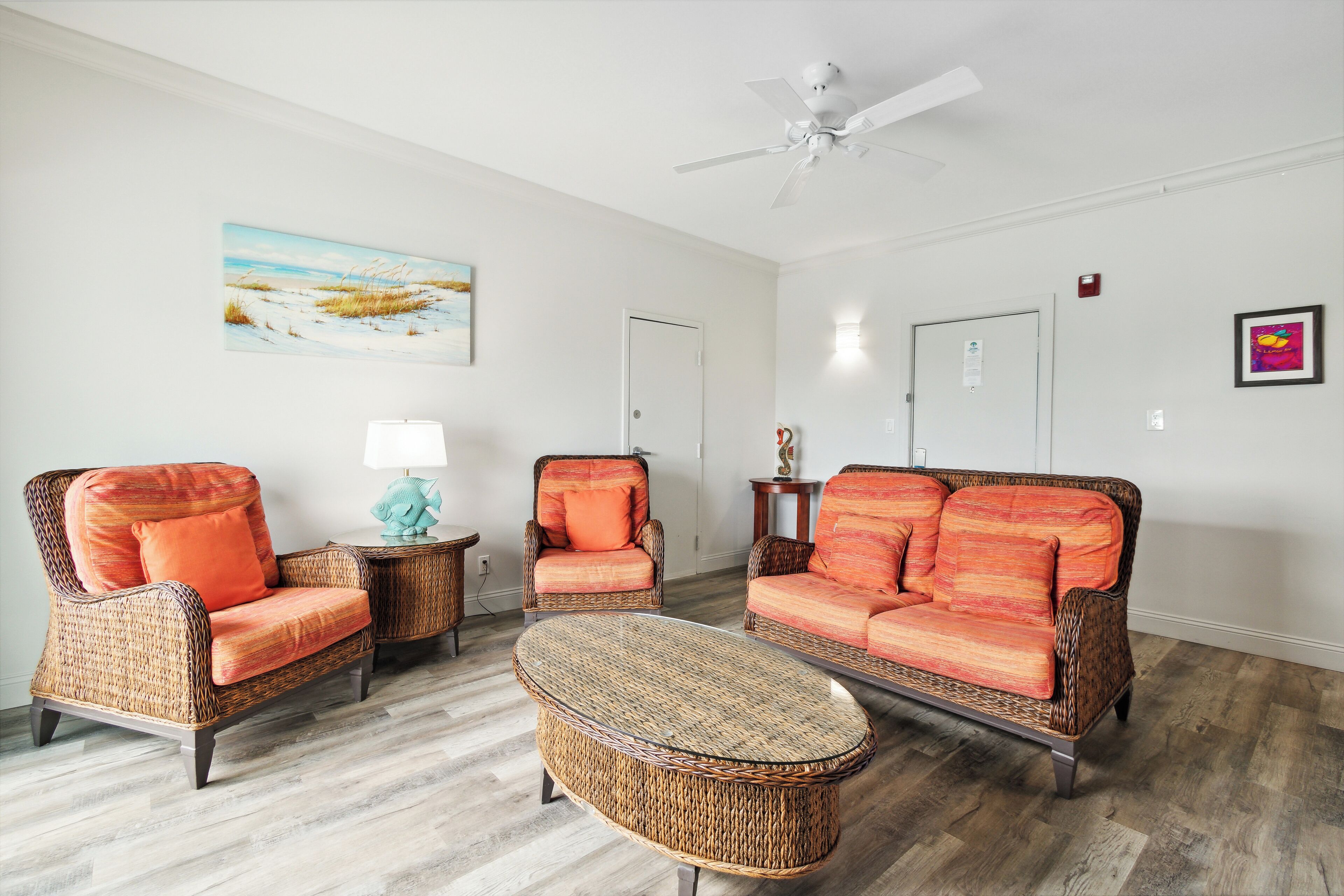 A living room with wicker furniture, a ceiling fan, and a painting on the wall.