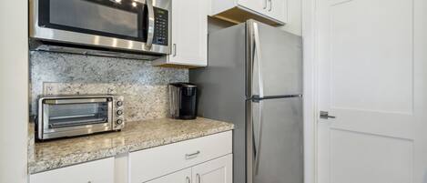 Una cocina con armarios blancos, un microondas de acero inoxidable, un horno tostador y un refrigerador.