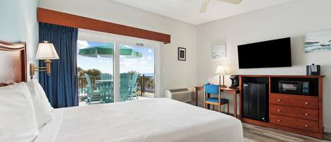 A hotel room with a large bed, a TV, a minibar, and a balcony with chairs and a table.