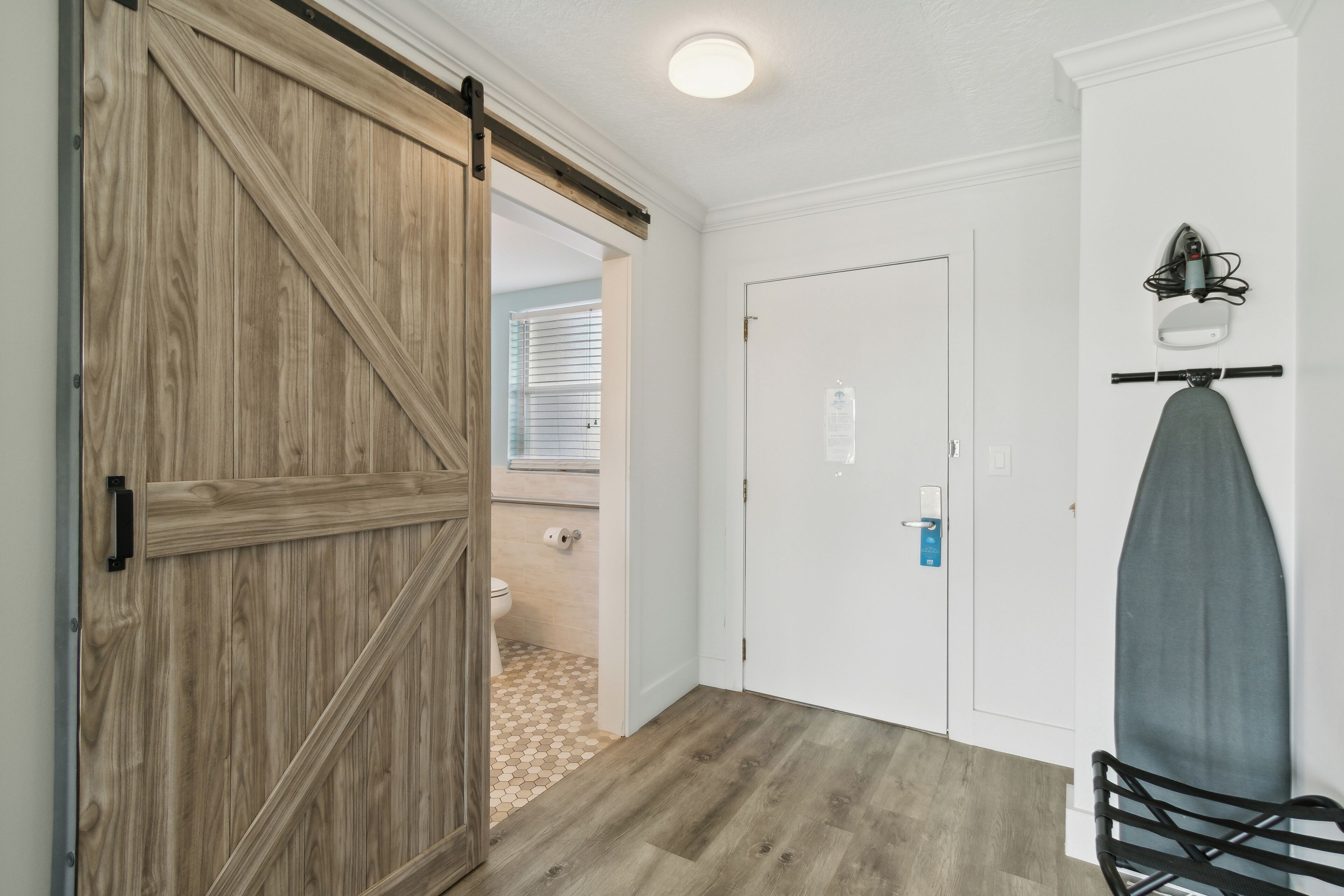 A hallway with a wooden sliding door, a white door, and a wall-mounted ironing board.