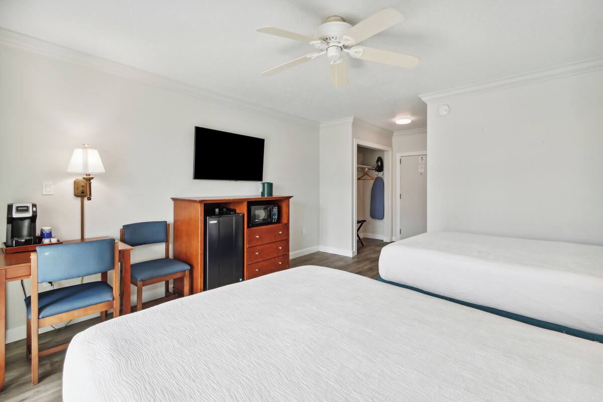 A hotel room with a bed, a desk with a chair, a wardrobe, a television, and a ceiling fan.