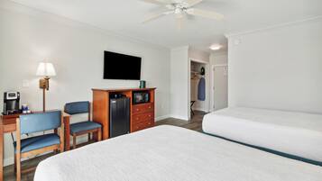 A hotel room with a bed, a desk with a chair, a wardrobe, a television, and a ceiling fan.