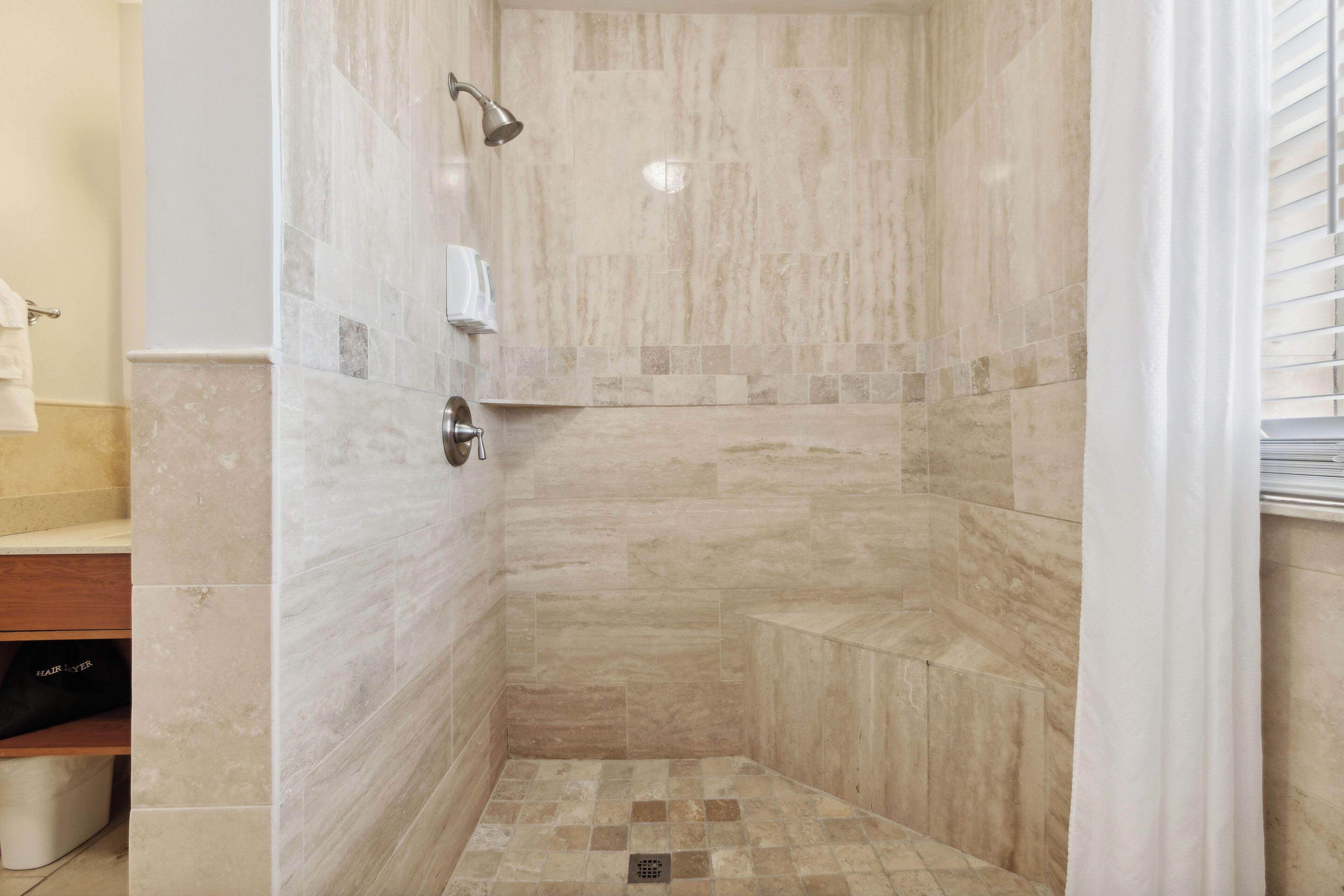 Ducha con azulejos color beige y cabezal de ducha manual.