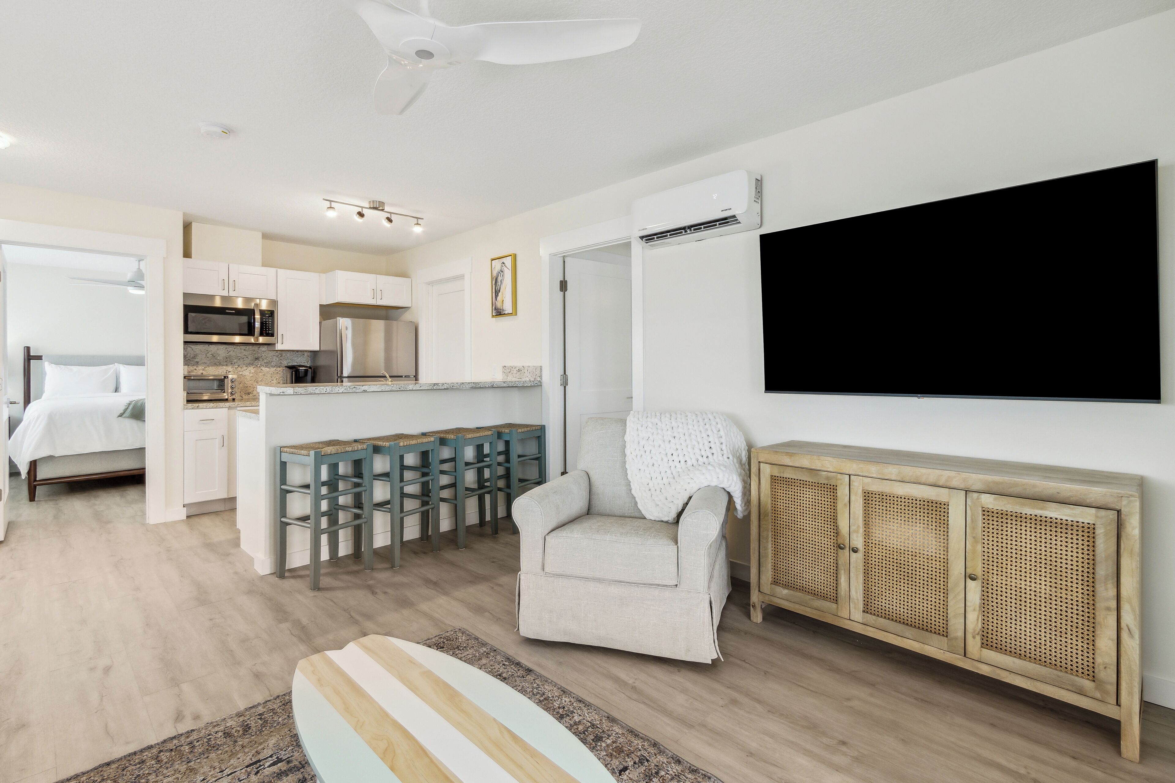 Una habitación moderna y luminosa con kitchenette, una zona de estar acogedora y un televisor de pantalla plana grande montado en la pared.