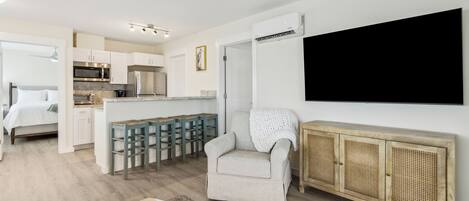 Una habitación moderna y luminosa con kitchenette, una zona de estar acogedora y un televisor de pantalla plana grande montado en la pared.