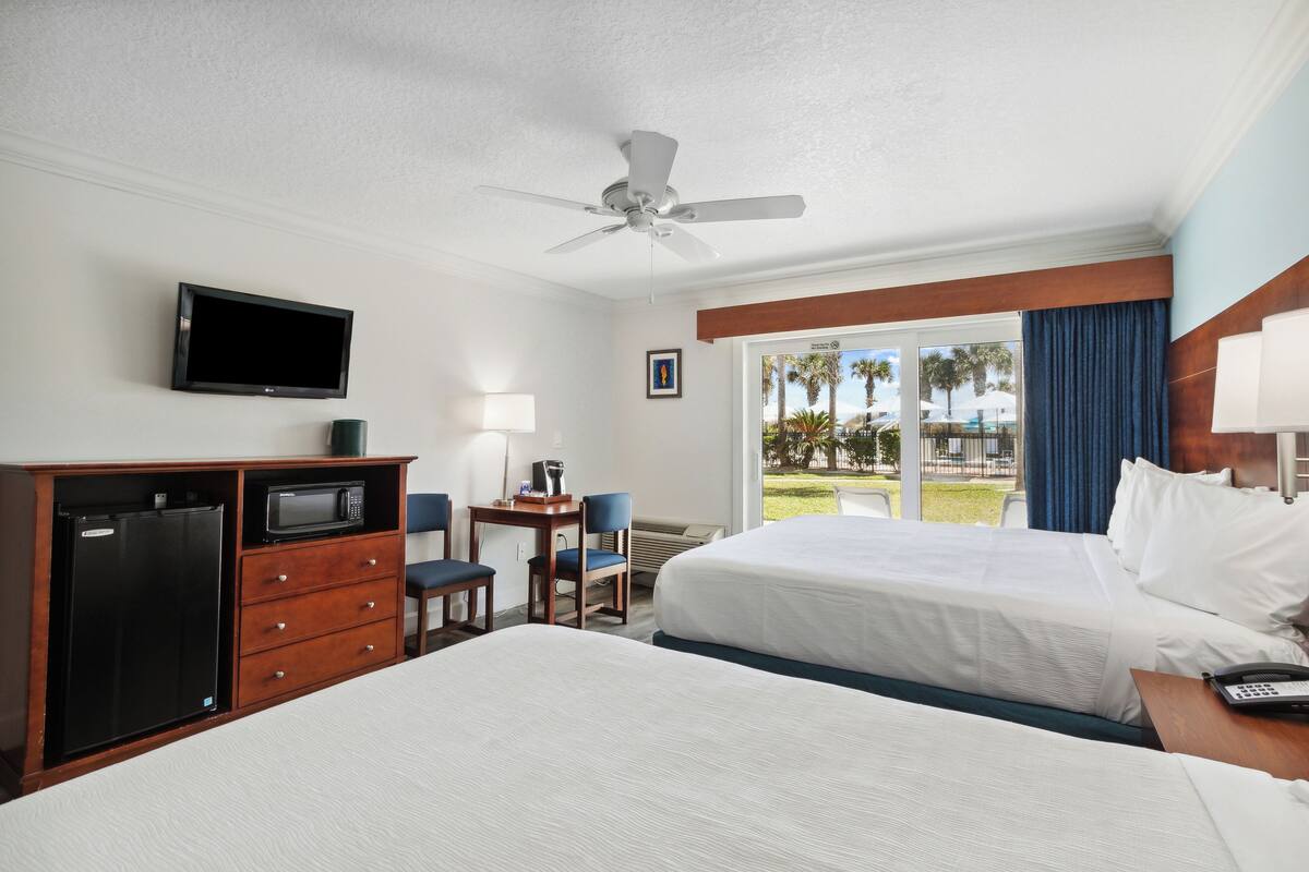 A hotel room with a bed, a desk with a chair, a microwave, a refrigerator, a television, and a view of the outdoors.