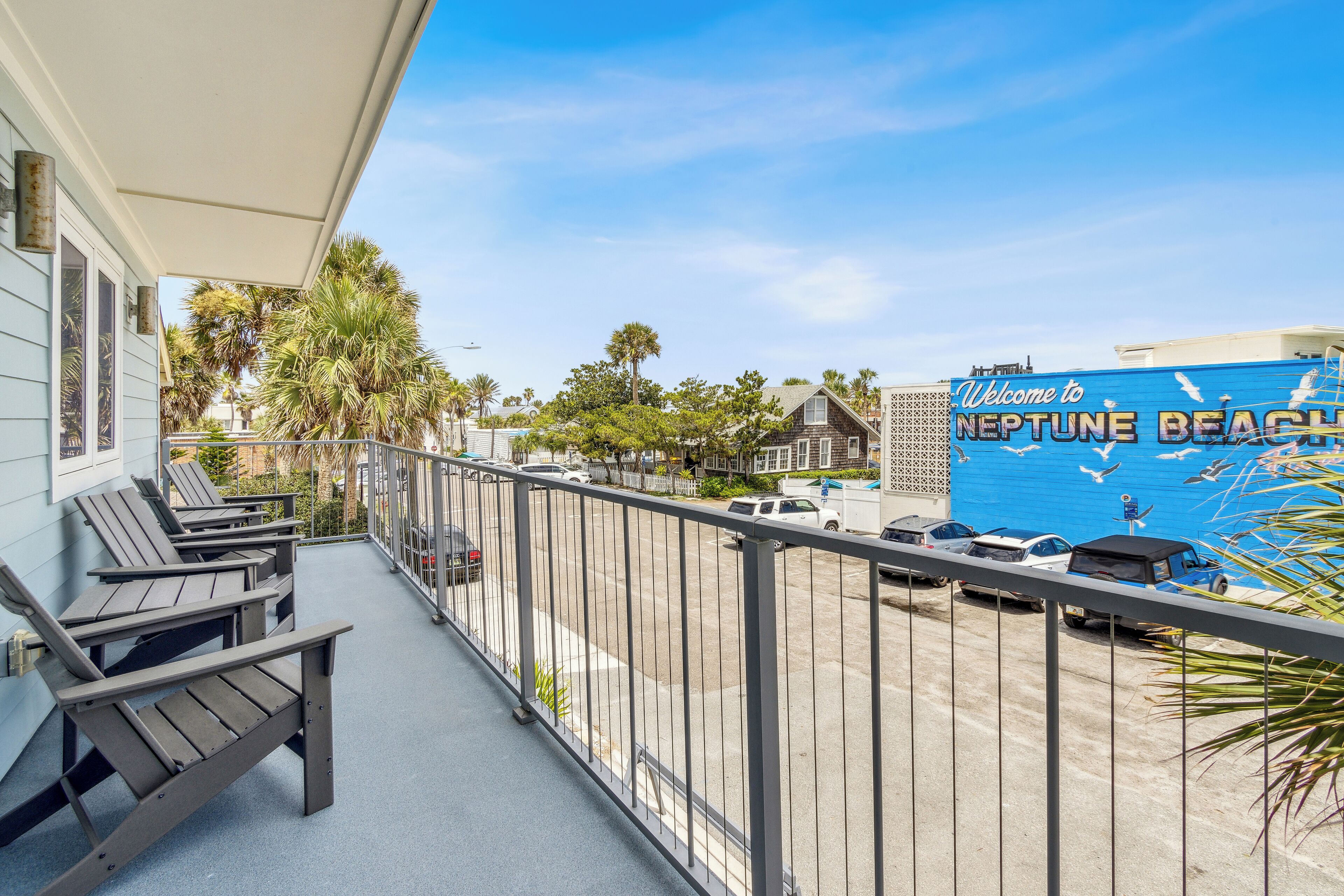 A balcony with Adirondack chairs, a view of Neptune Beach, and parked cars.