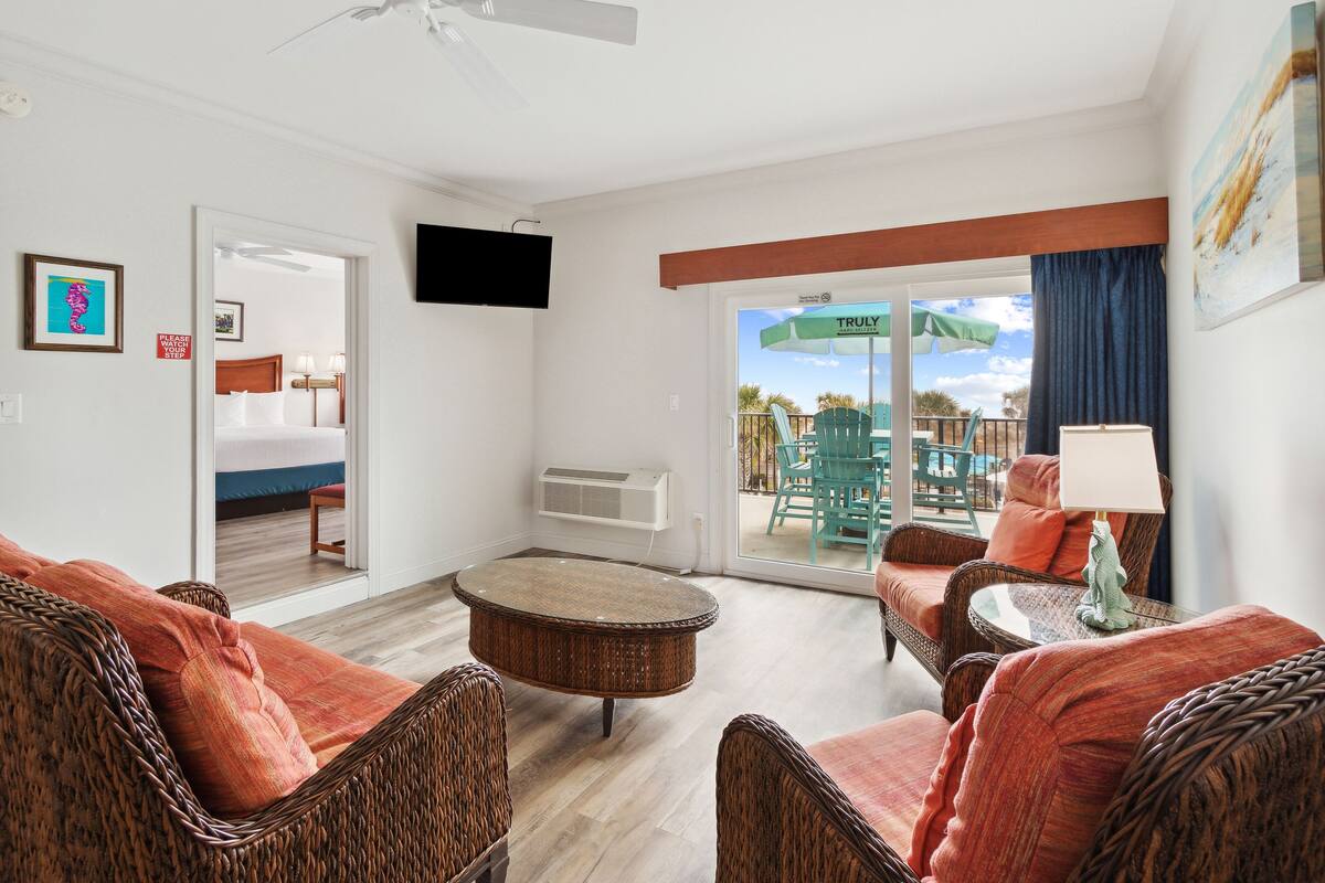 A hotel room with wicker furniture, a round coffee table, and a view of the outdoor area.